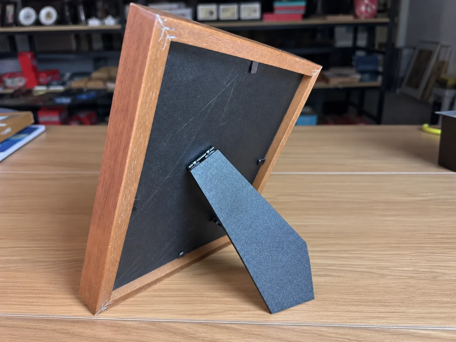 A framed piece seen from behind, standing on a desk on its open fold-out stand.