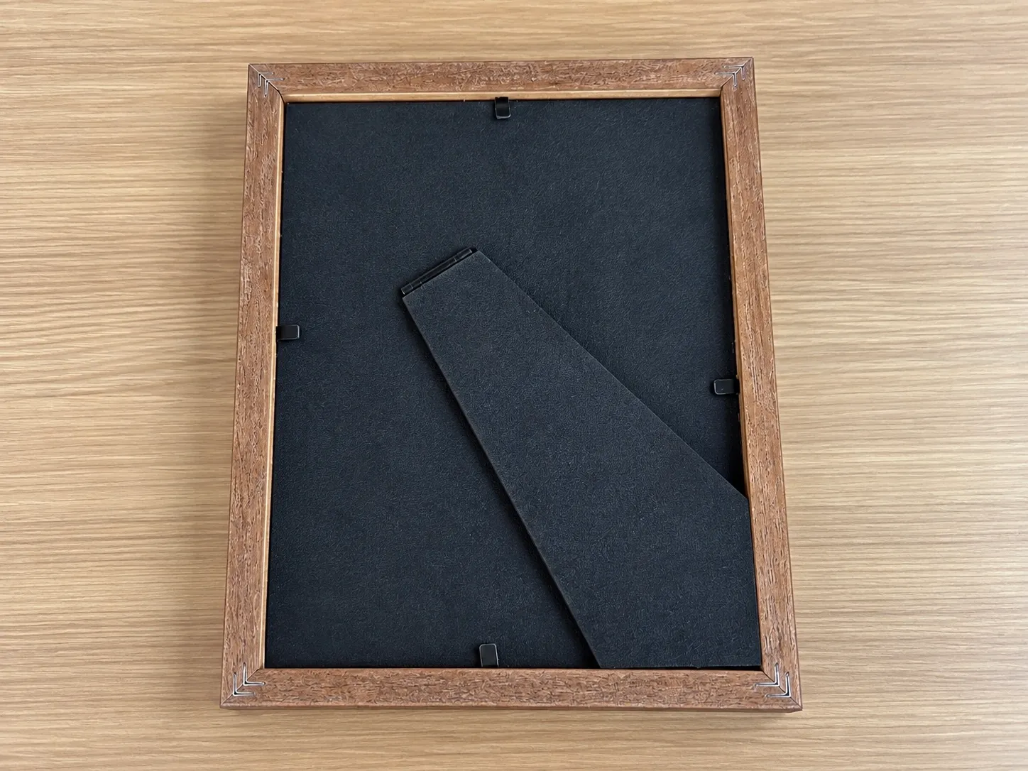 The back of a wood frame with a black back panel held in by clips, and a fold-out stand.
