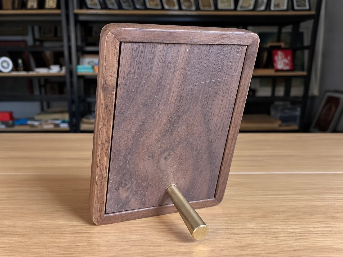 A small framed piece with a solid wood back panel, standing on a brass-tone pin.
