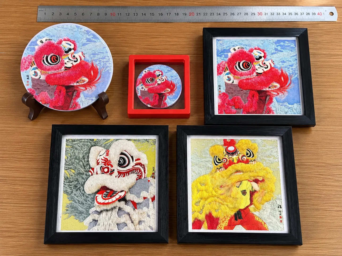 A lion-dance series laid out with a 40 cm steel rule: a disc on a stand, a small round piece in a red box and three framed pieces.