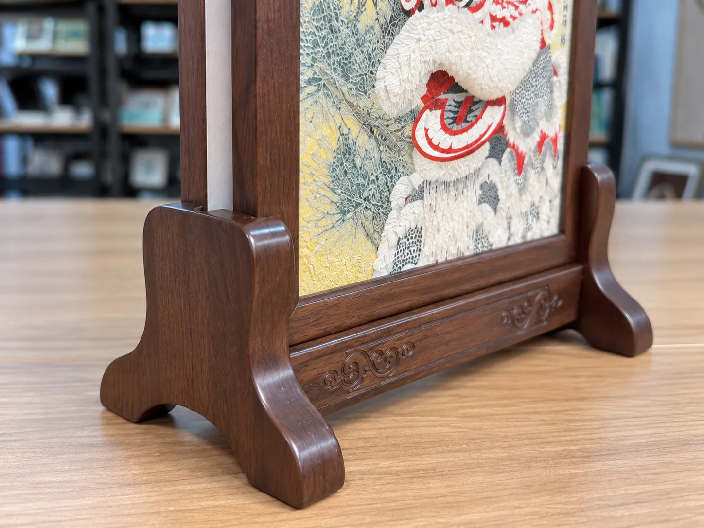 Close view of a dark wood table-screen base with scroll-pattern detail and the slot the panel stands in.