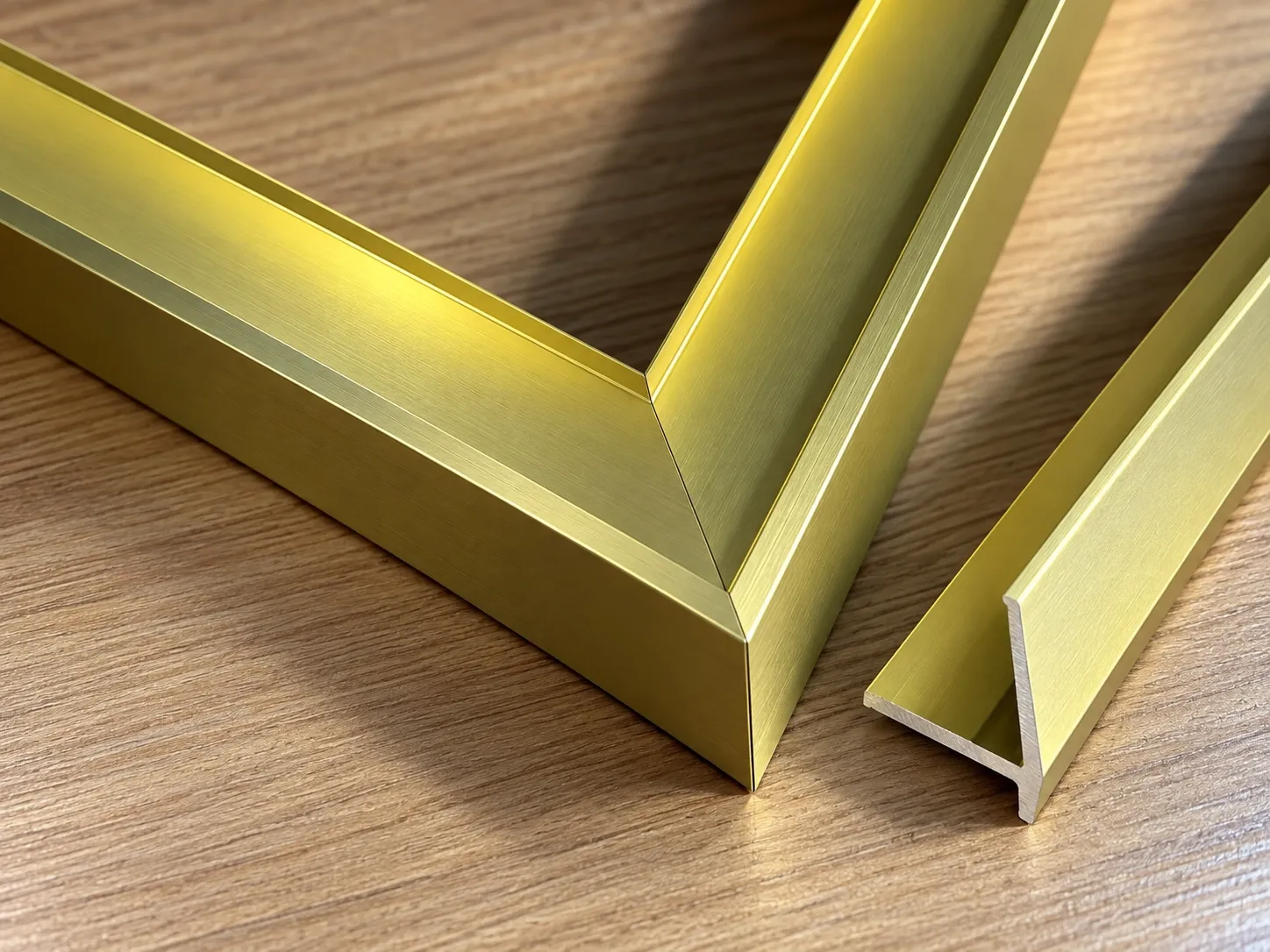 An aluminium alloy frame corner in a brushed gold-tone finish beside a length of the profile.