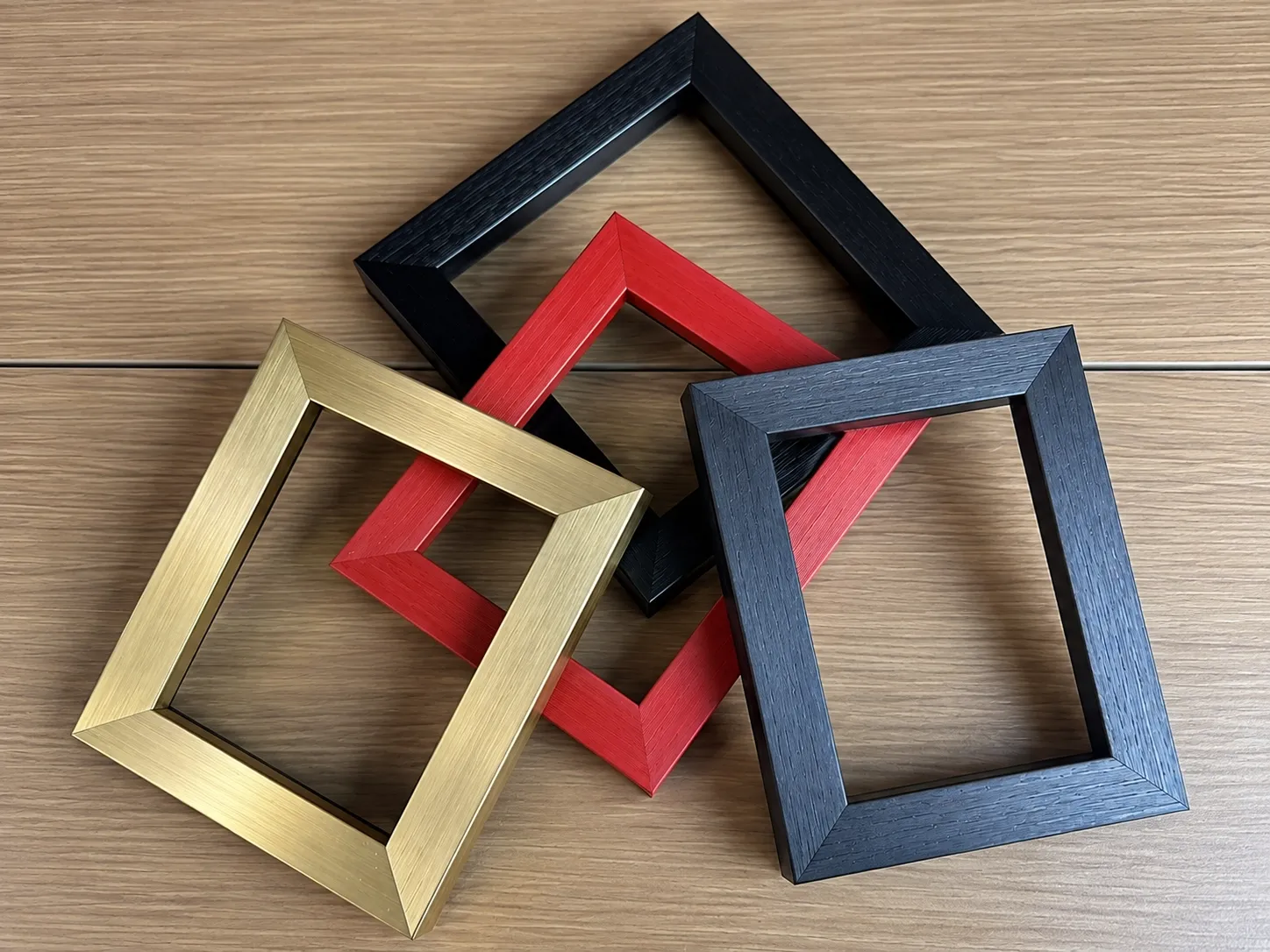 Four empty frames in brushed gold, red, black and charcoal finishes.