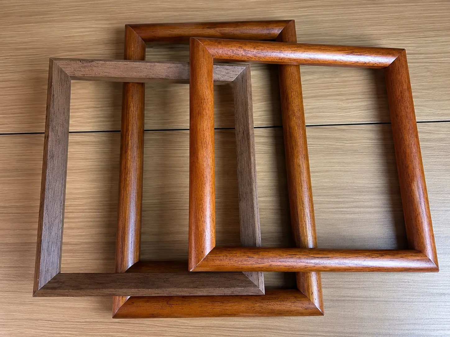 Three empty wood frames in orange-brown and grey-brown finishes, two with rounded profiles.