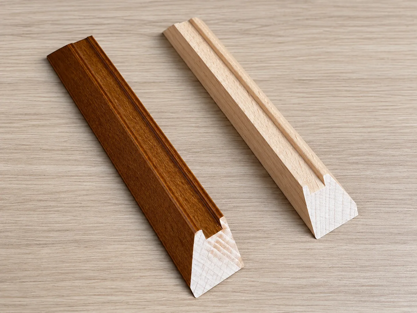 Two lengths of wood frame moulding, one stained and one natural, cut ends showing the profile.