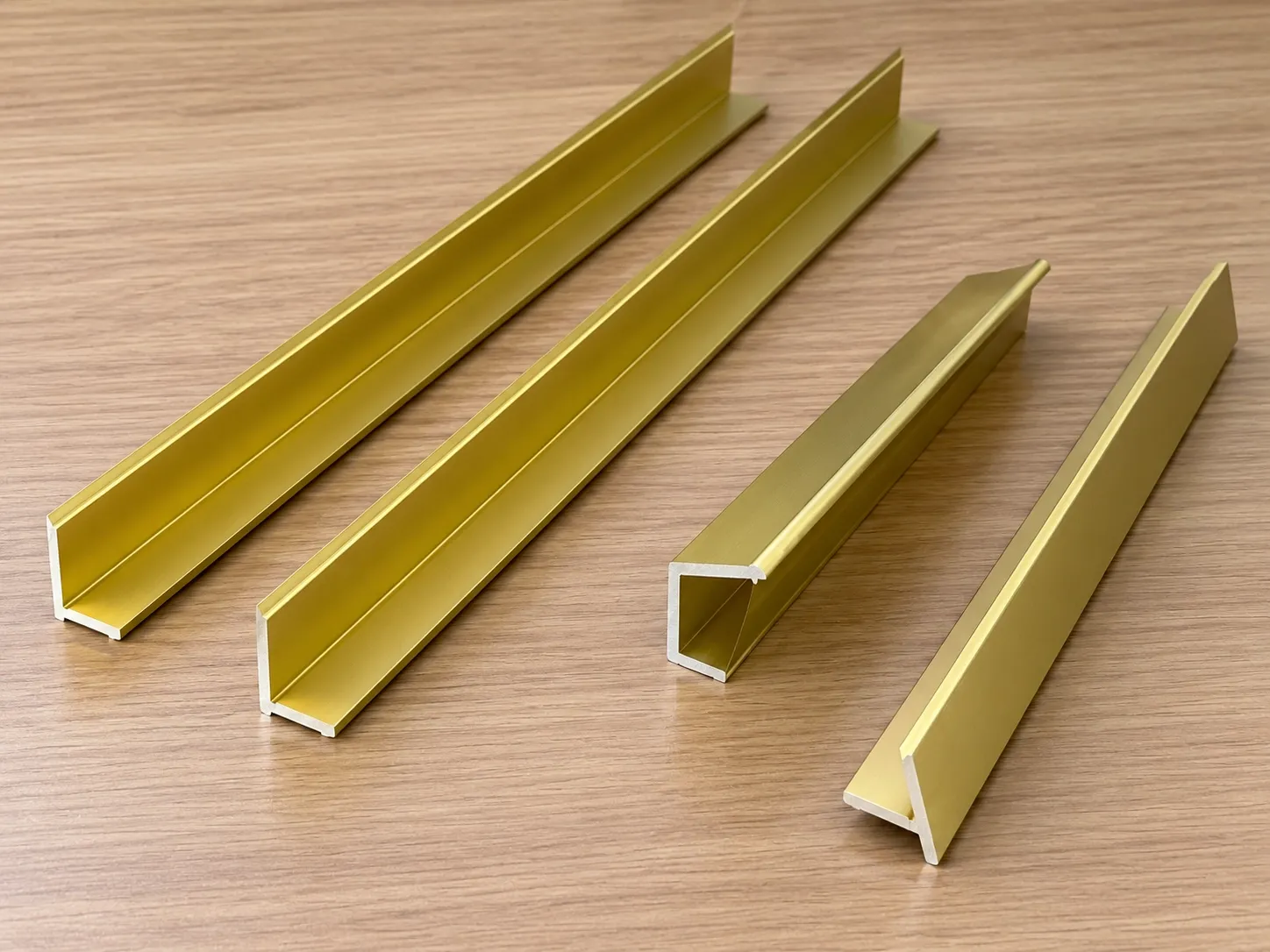 Four aluminium alloy frame profiles in a gold-tone finish, ends showing their sections.