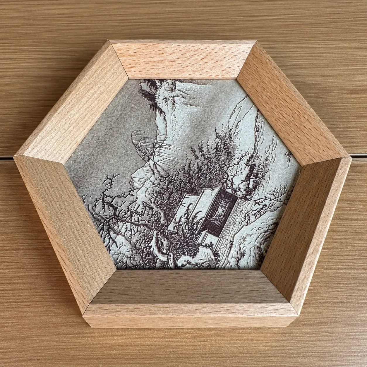 A hexagonal natural wood frame around a monochrome ink-landscape piece.