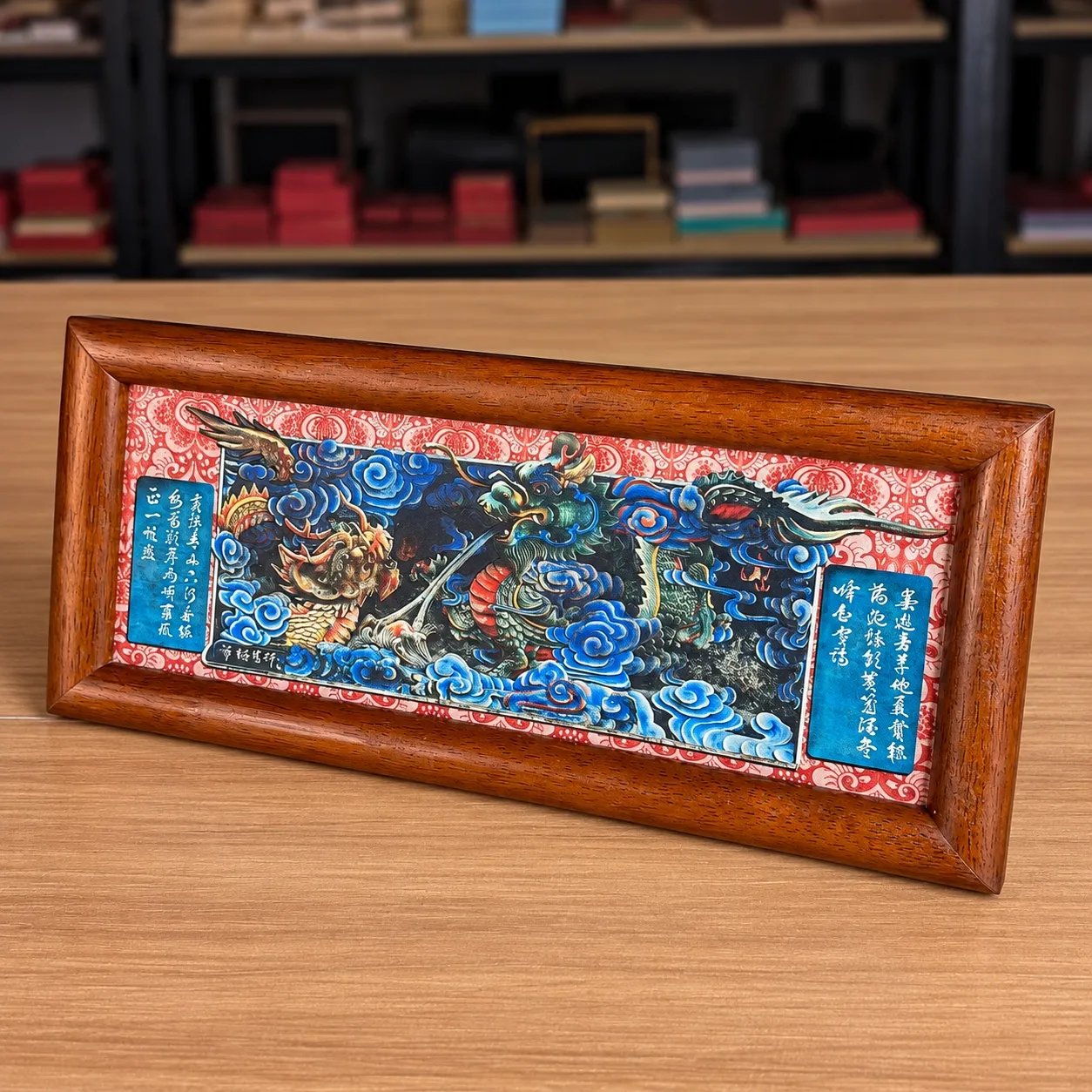 A long landscape-format piece with a dragon among blue clouds and calligraphy panels, in a rounded reddish wood frame.