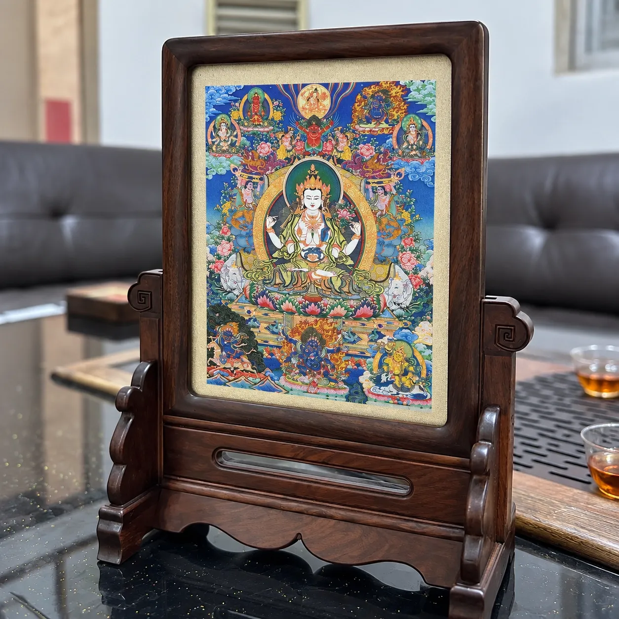 A Thangka piece of Four-Armed Avalokiteshvara held in a dark wood table-screen stand on a tea table.