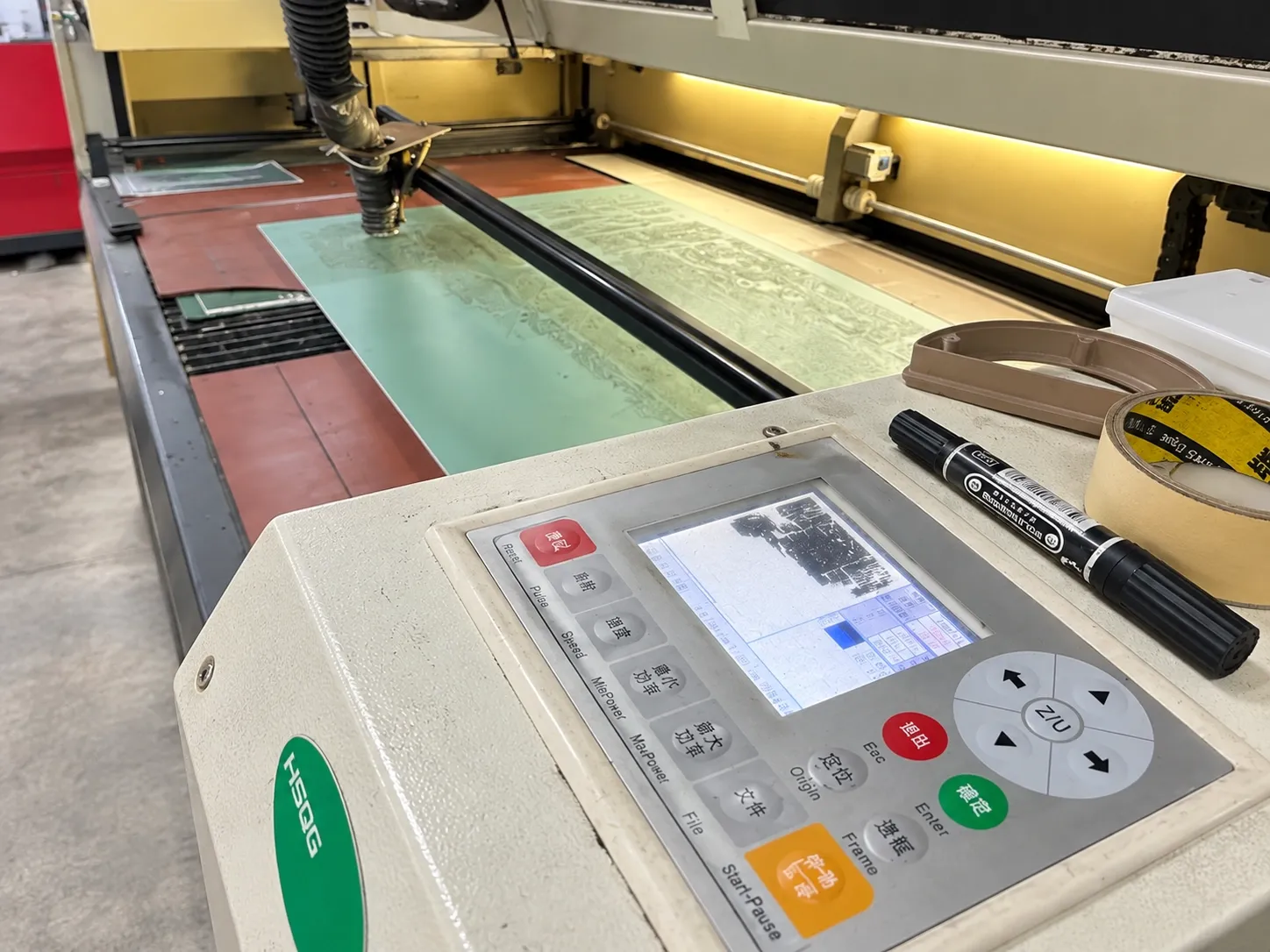 A laser cutter control panel showing the cut file on screen, with film-covered panels on the bed behind.