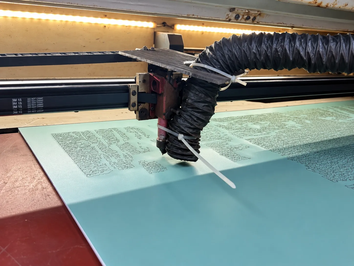 A laser head with a fume extraction hose cutting a pattern into film on a panel.