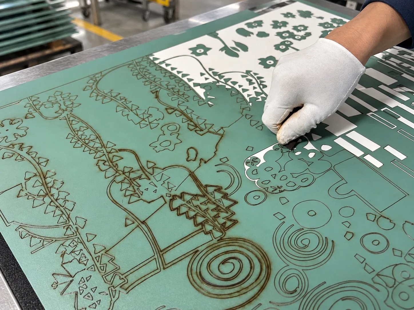 A gloved hand lifting cut sections of resist film from a patterned panel.