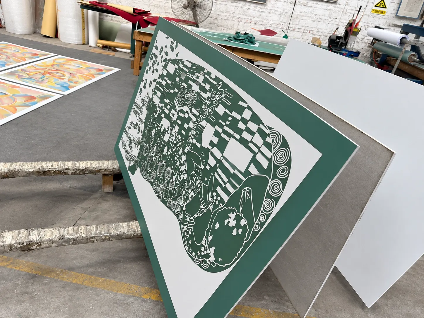 A full-size panel leaning against others, its resist film cut and weeded into one detailed figurative design.