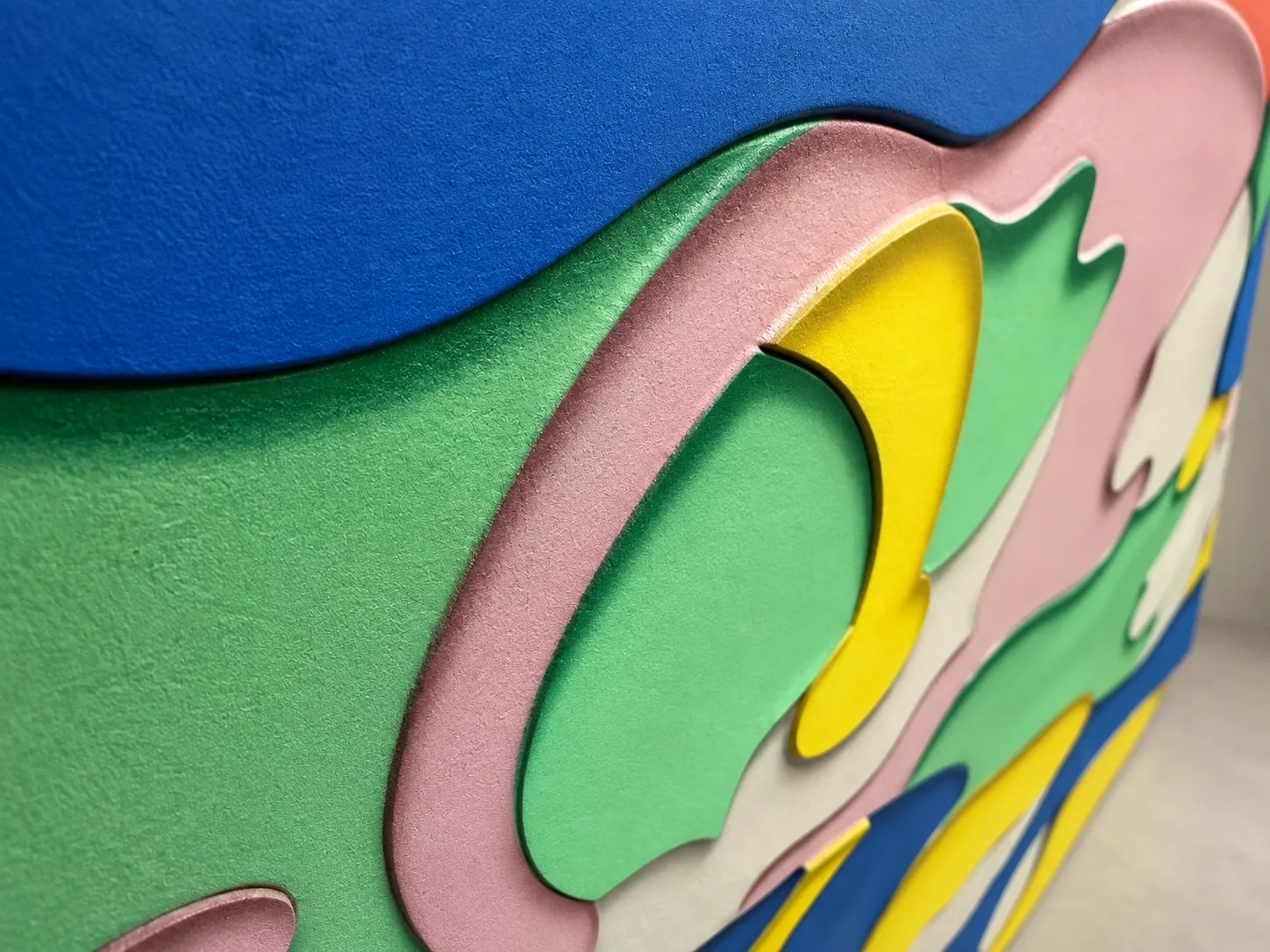 Abstract ceramic relief of blue, green, pink and yellow shapes stepping down in distinct levels.