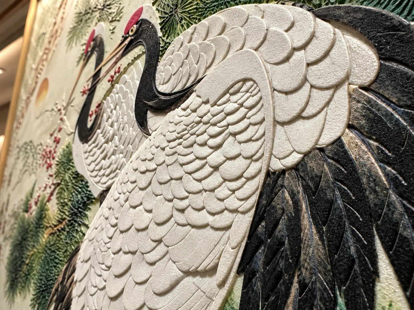 Angled view of a large relief mural of red-crowned cranes, each feather a raised overlapping form.
