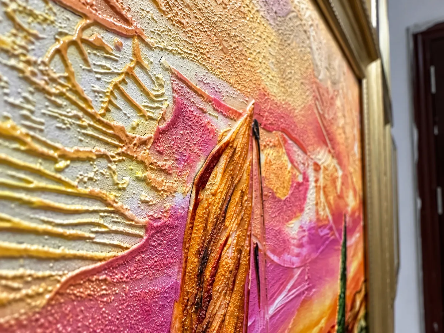 Angled view of a framed sunset picture with raised, glossy impasto texture across its surface.