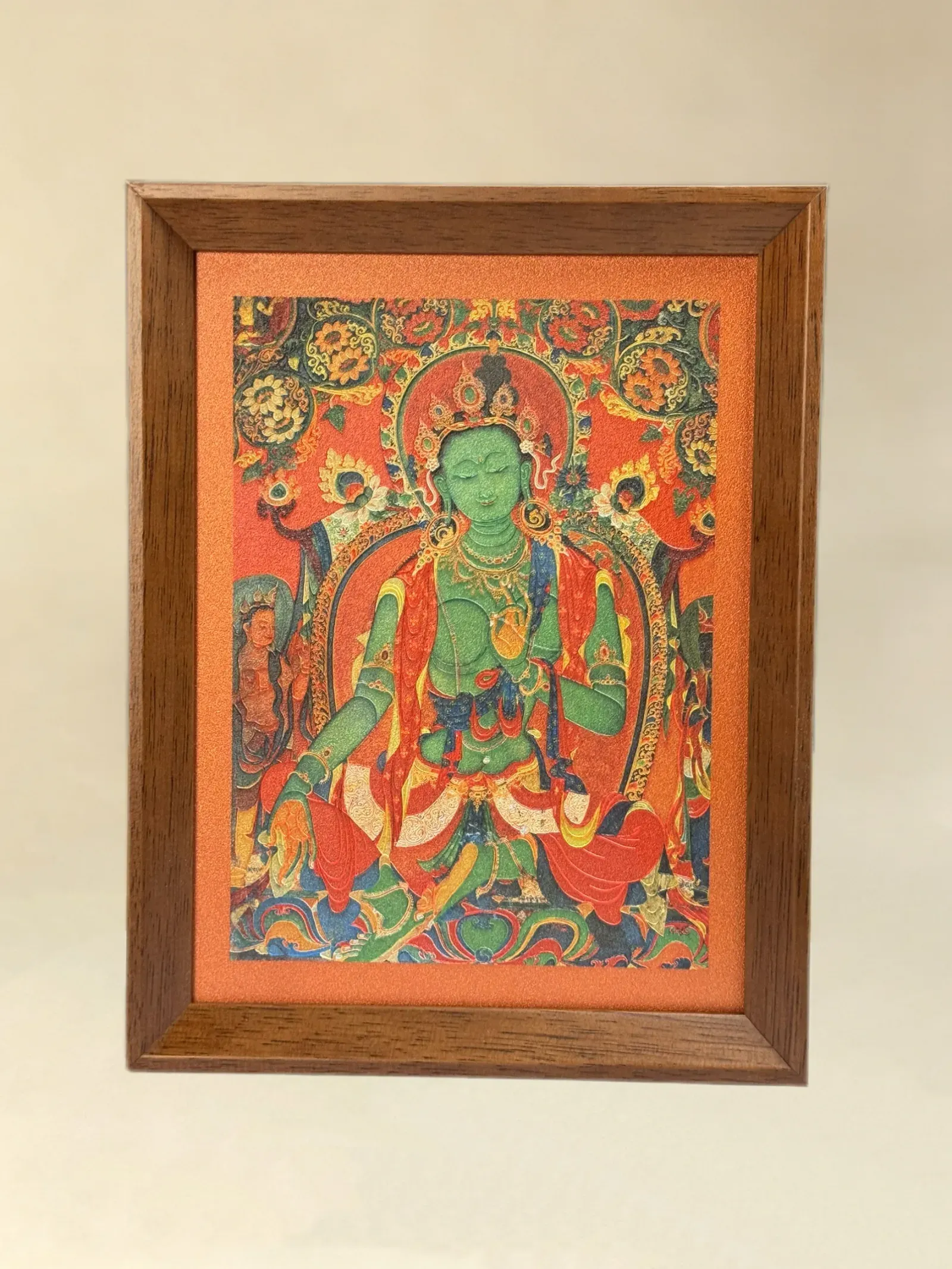 A relief artwork of Green Tara, red ground, as a desktop frame, photographed front on.