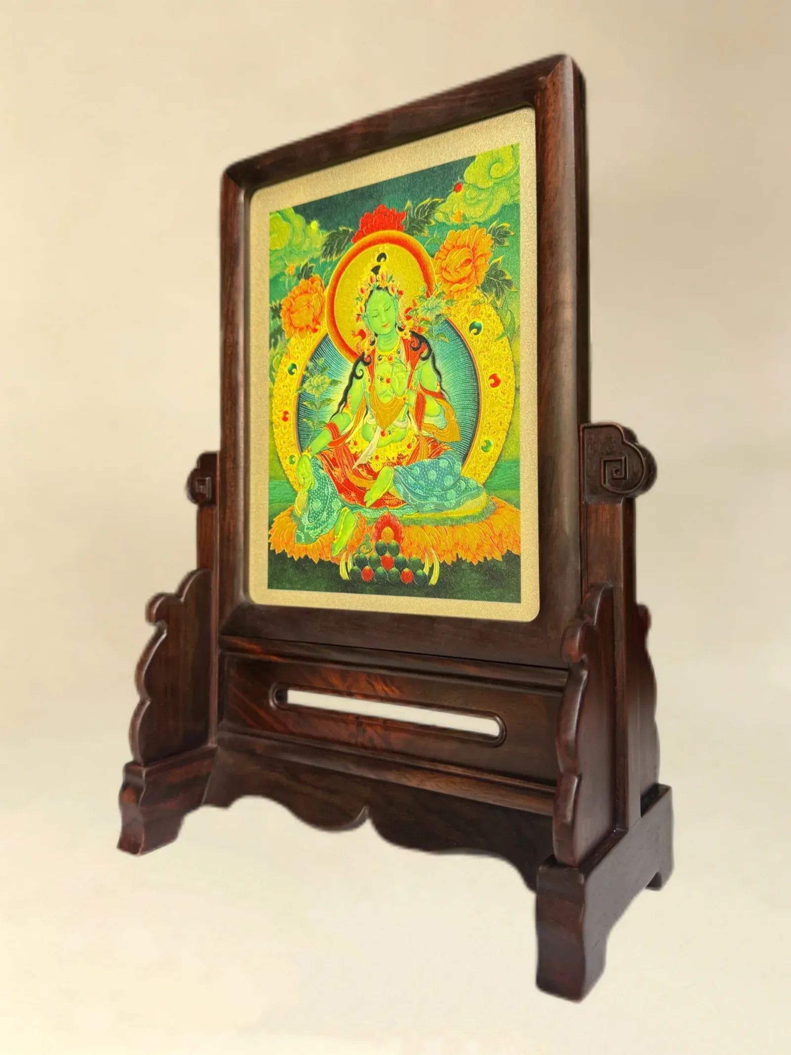 A Green Tara relief panel in a table-screen stand, seen at an angle so light falls across the raised outlines.