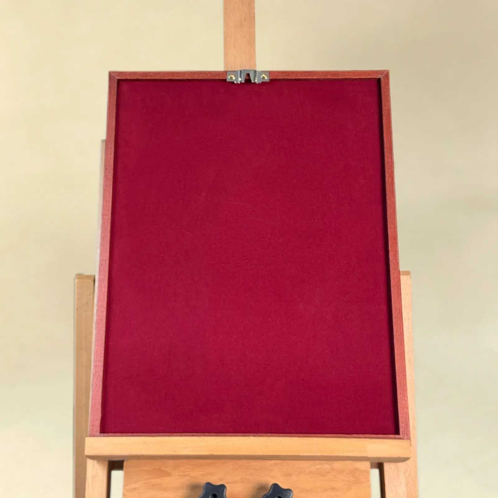The back of a framed wall piece on an easel: a deep red fabric-covered back with a hanging fixing at the top.